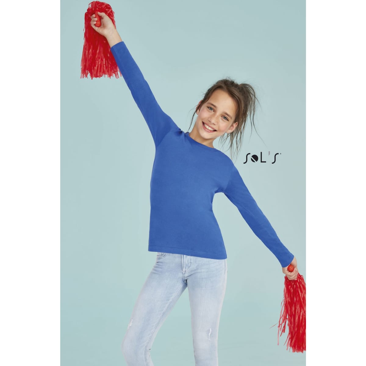 A bright blue long sleeve T-shirt made from 100% semi combed ring spun cotton, worn by a smiling girl with red pom-poms.