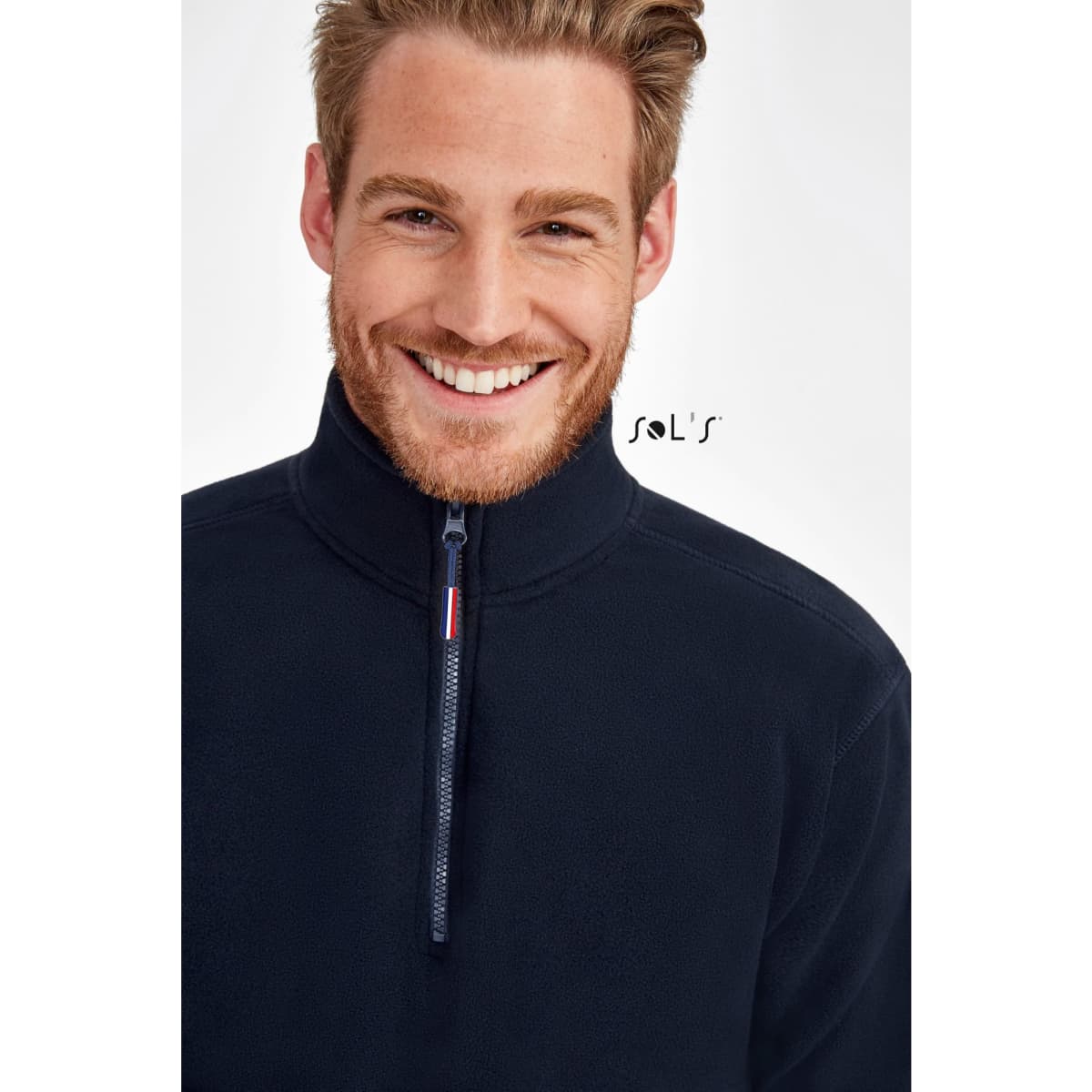 A smiling man wearing a navy blue zip-up fleece pullover with a high collar and a logo on the side.