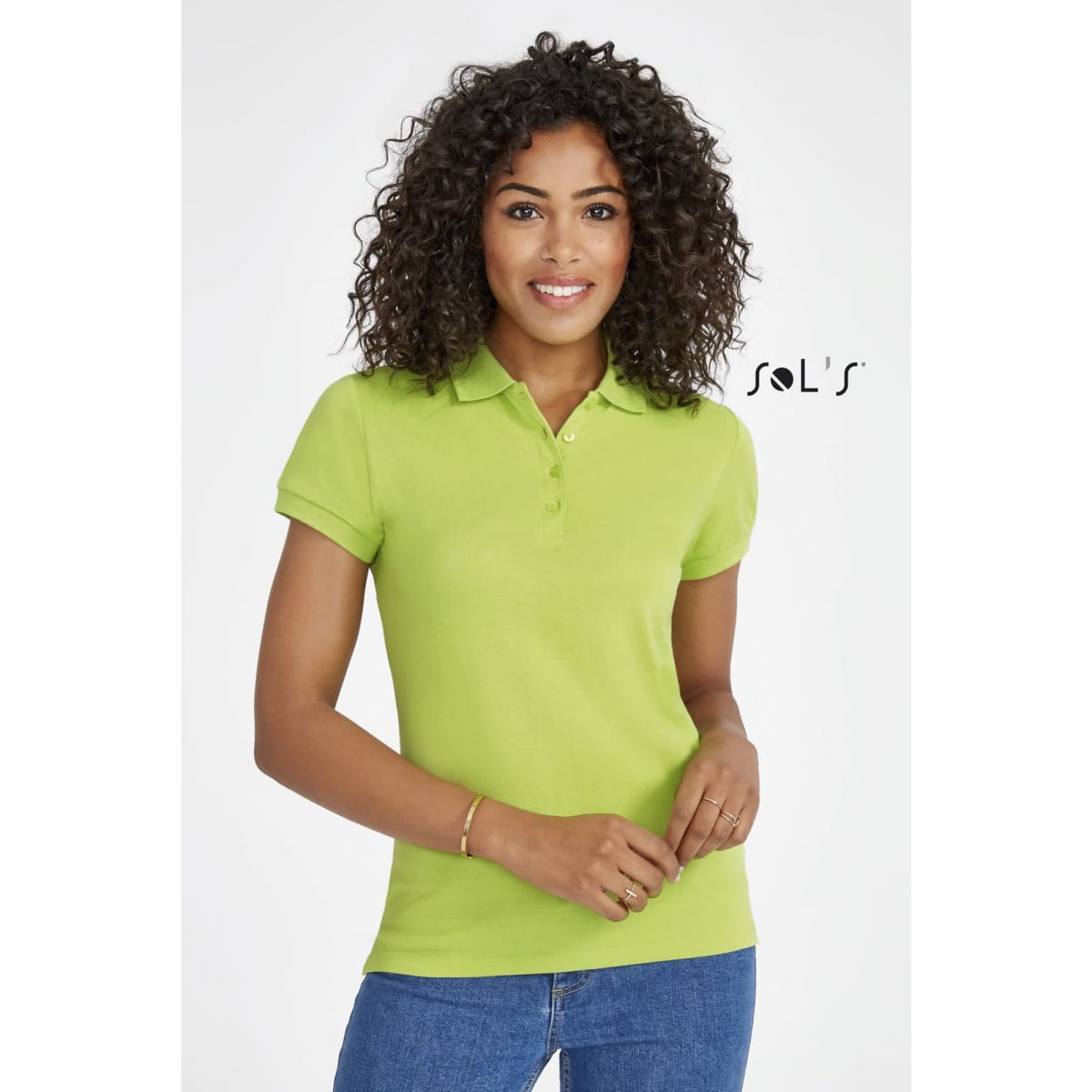 A woman wearing a bright green polo shirt made of 100% combed ring spun cotton. The shirt has a logo on it.