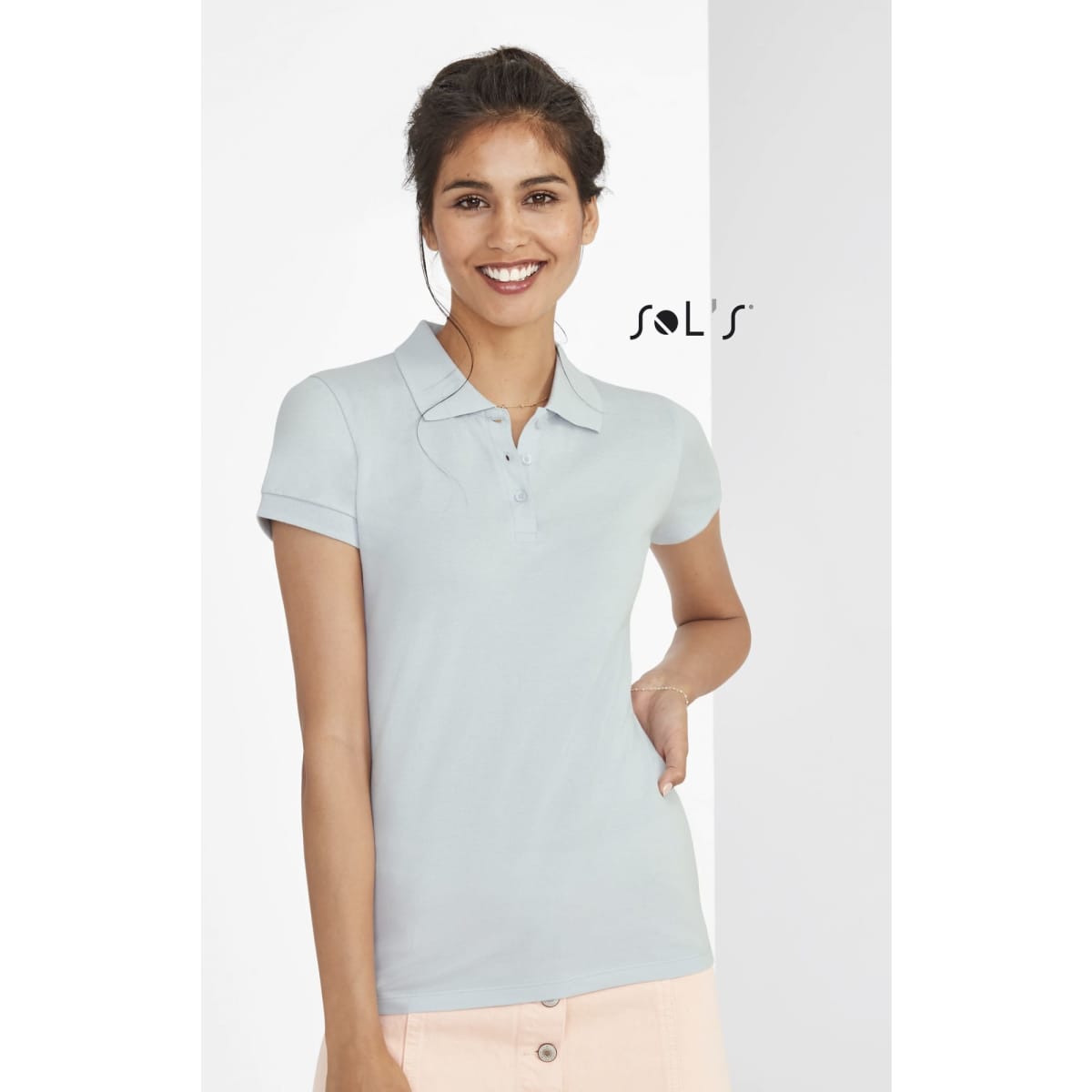 A women's polo shirt in light blue, made from 100% cotton pique, featuring a logo on the upper left.