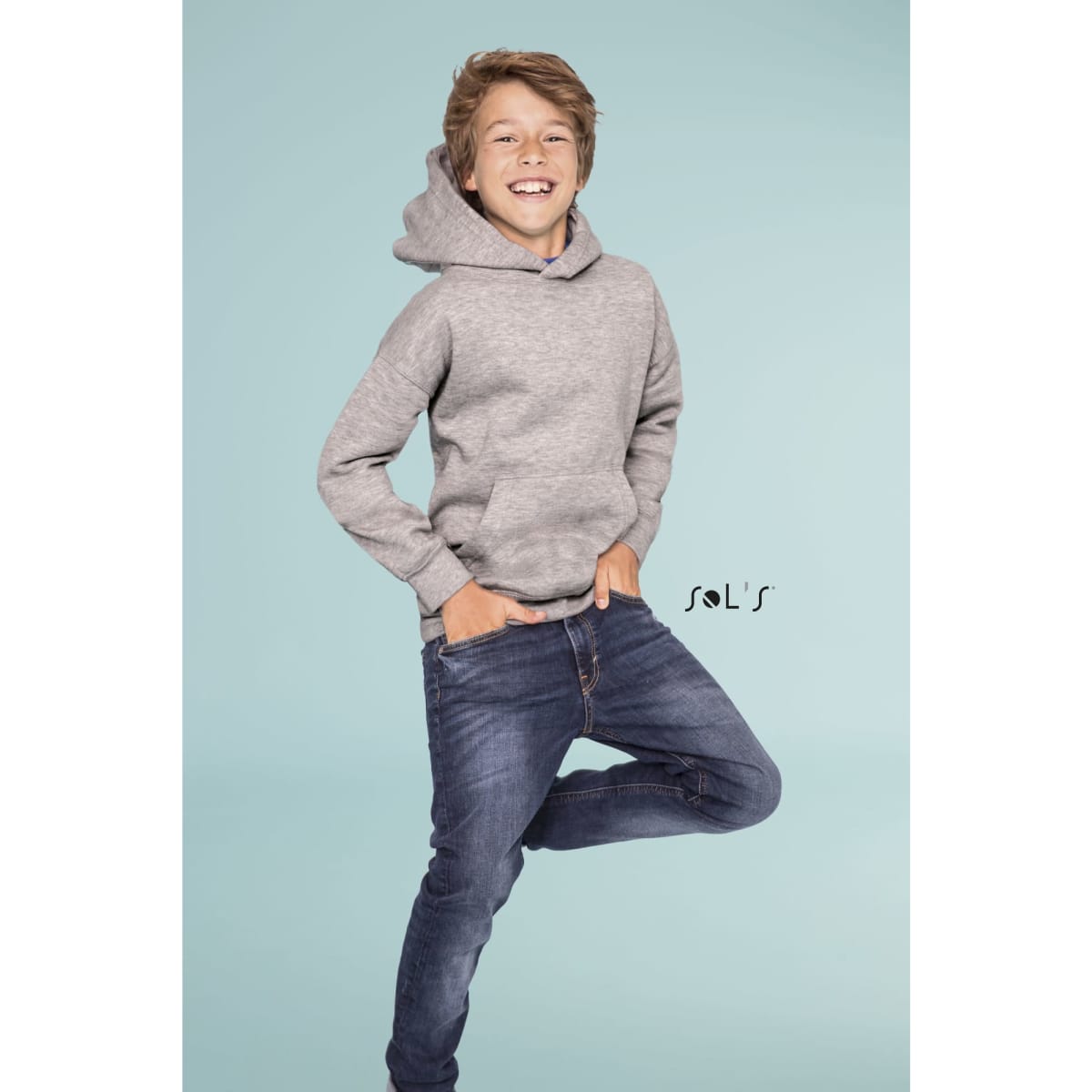 A grey hoodie with a hood worn by a smiling boy, standing in a playful pose with hands in pockets.