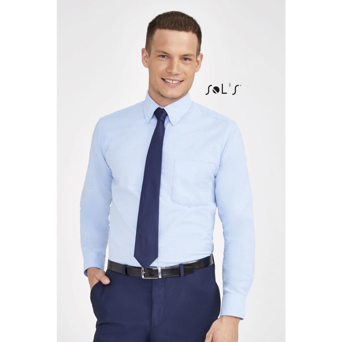 A light blue long sleeve oxford shirt with a pocket, paired with a dark tie and belt, worn by a model.