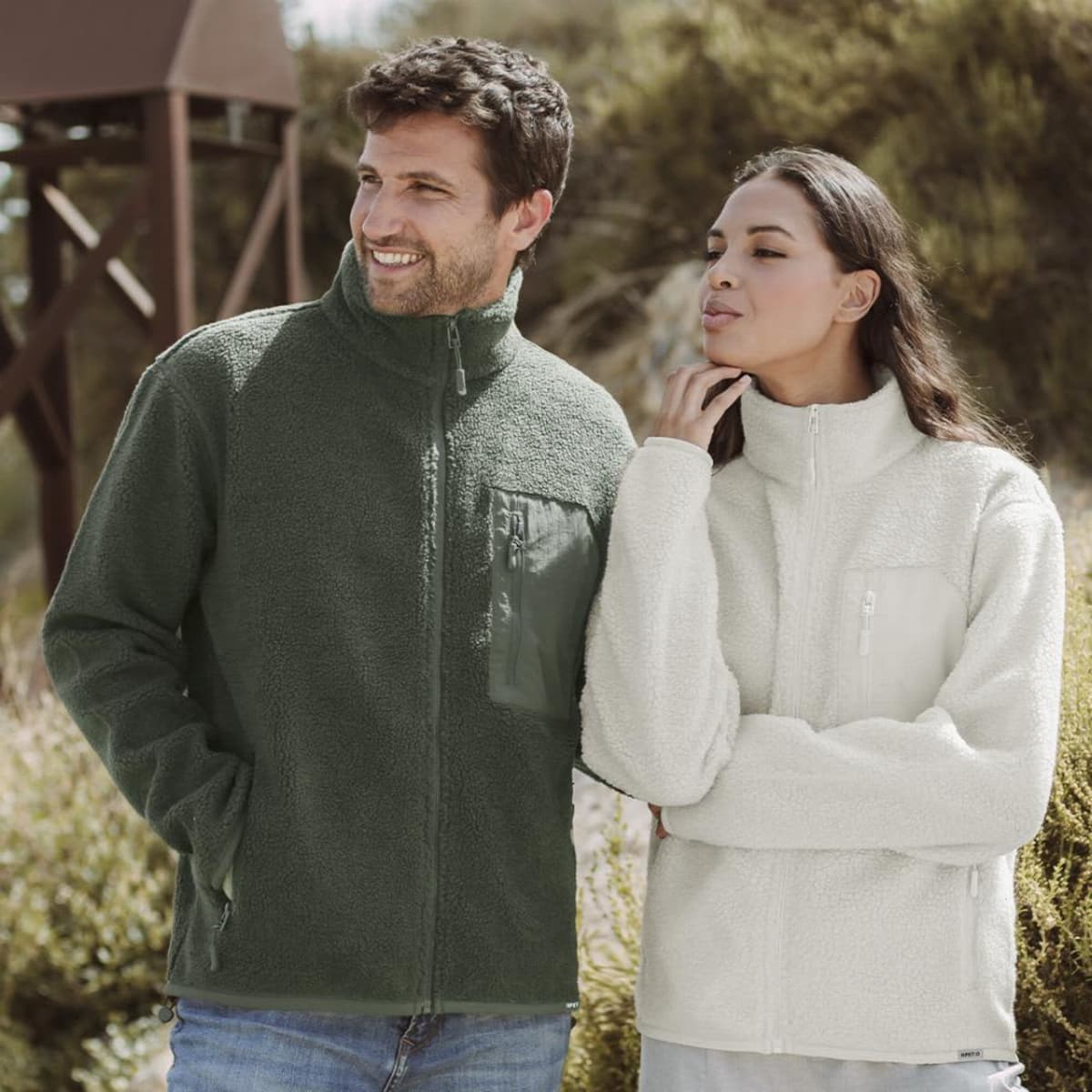 A green fleece jacket and a cream fleece jacket worn by a man and woman outdoors. Both jackets feature zip closures.