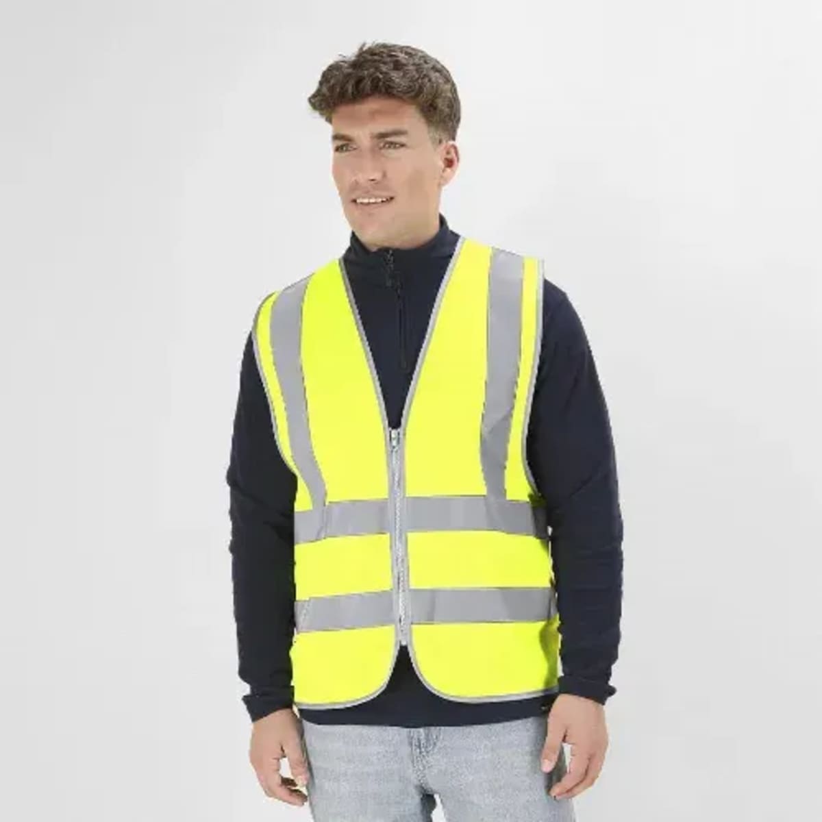 A high-visibility safety vest in bright yellow with reflective grey stripes, worn by a man standing against a plain backdrop.