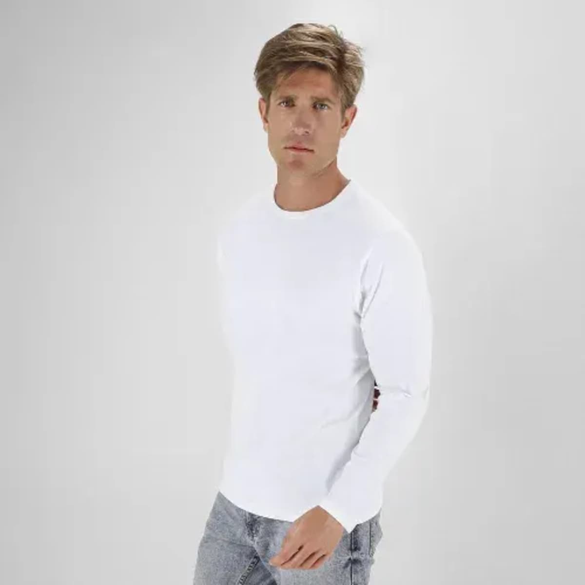 A casual white long-sleeve shirt worn by a man, paired with light grey jeans. The model stands against a plain background.