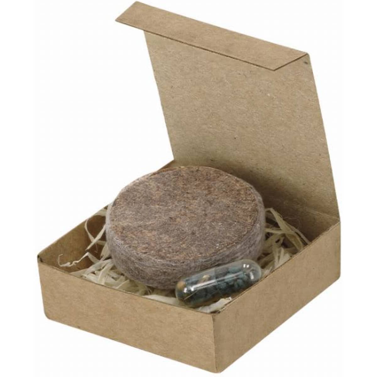 A gift box containing a round, brown product and a transparent capsule, resting on shredded paper.