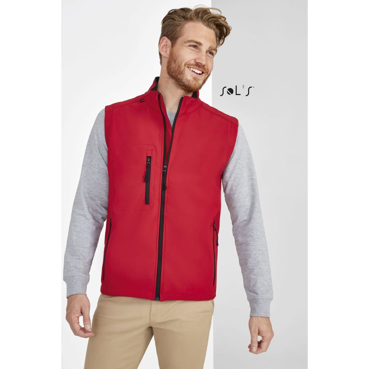 A red softshell vest with a zip front and pockets, worn over a grey long-sleeve shirt. It features a logo.
