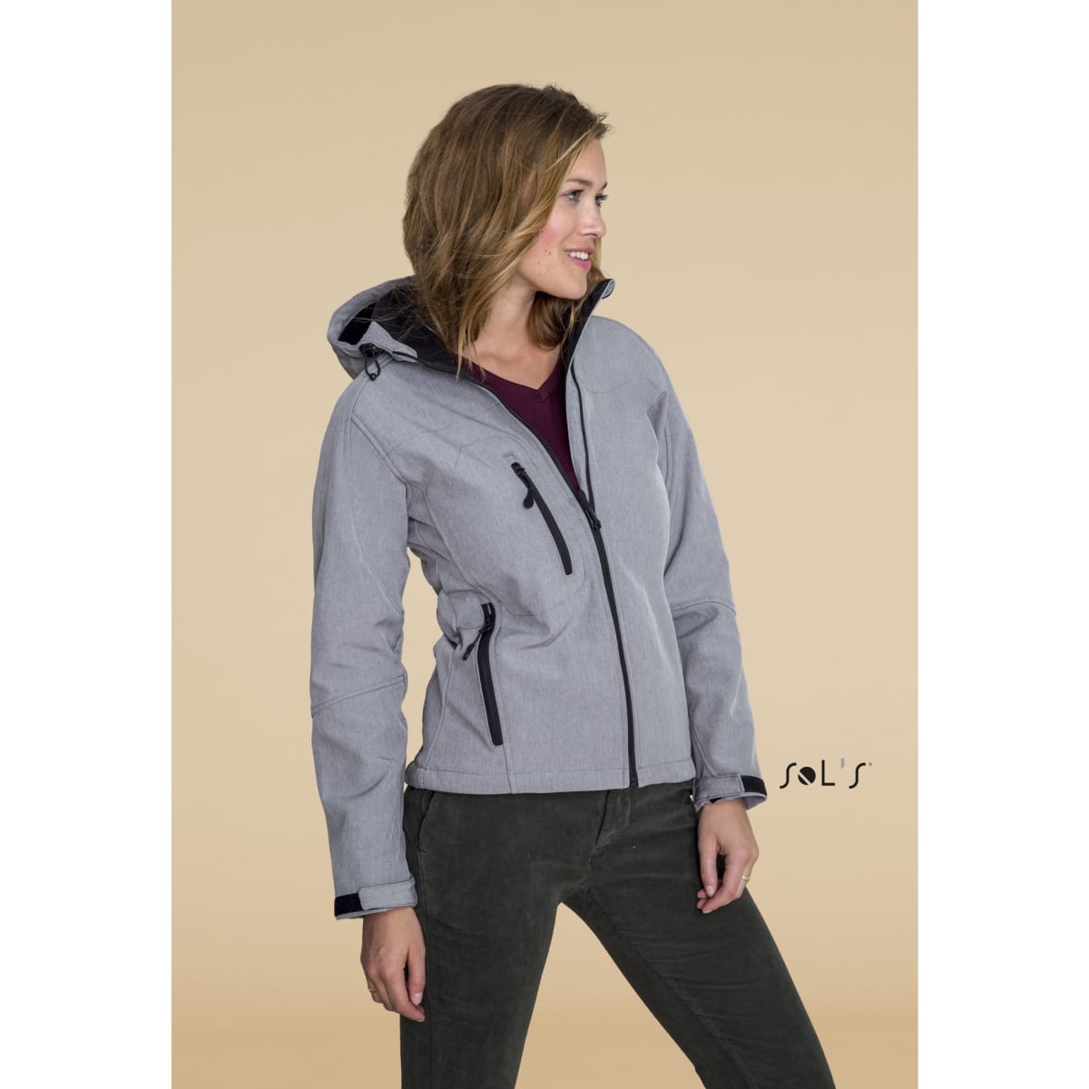 A woman wearing a grey softshell jacket with a hood, featuring black accents and a branded logo.