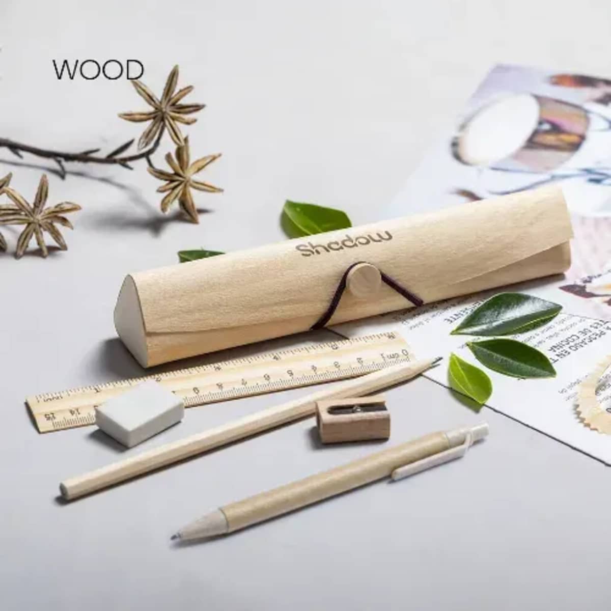 A wooden stationery set including a pencil case, ruler, pencil, eraser, sharpener, and pen, with leaves and paper nearby.