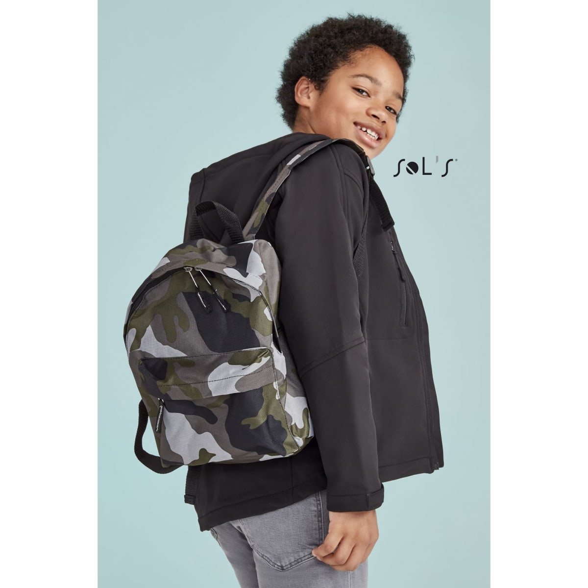 A child wearing a camouflage rucksack, featuring a logo, against a light blue background.