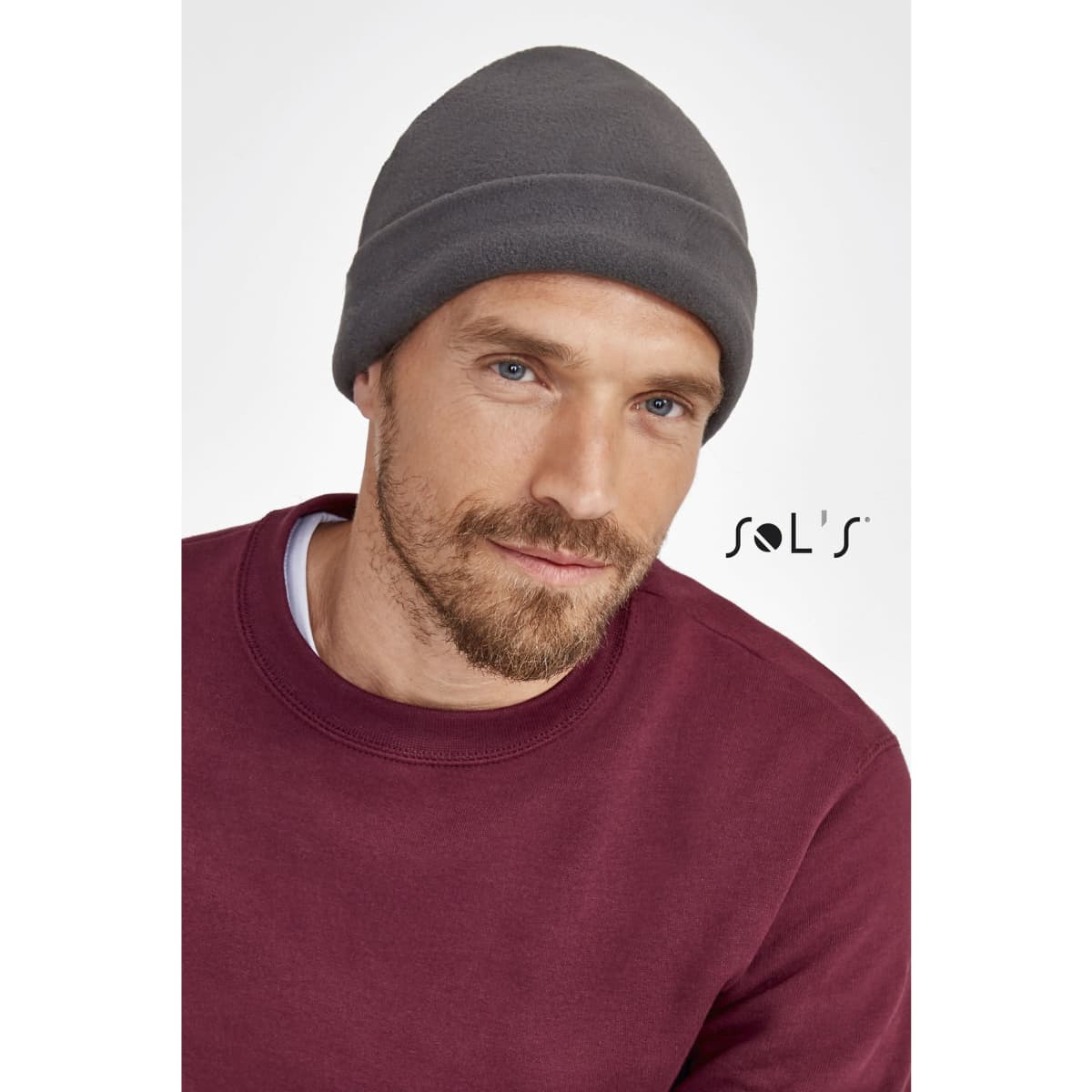 A grey fleece beanie worn by a man with a beard, paired with a maroon sweatshirt. The image features a logo.