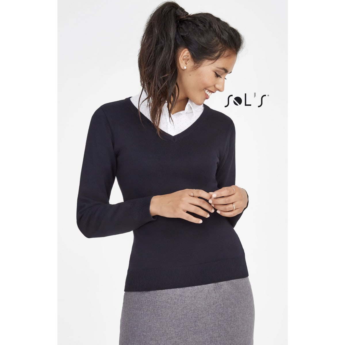 A navy women's V-neck jumper with long sleeves, paired with a collared shirt and grey skirt. Features a logo.