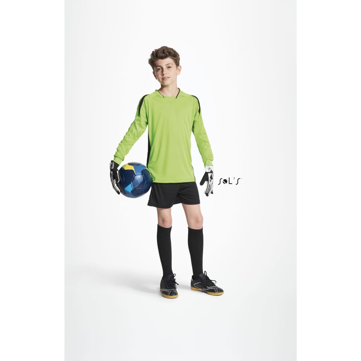 A kid wearing a green goalkeeper shirt, black shorts, and gloves, holding a soccer ball.