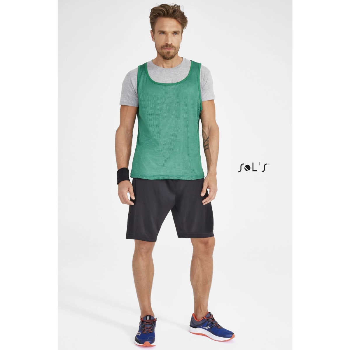 Green sports bib worn over a grey t-shirt, paired with black shorts and sports shoes. Includes a visible logo.