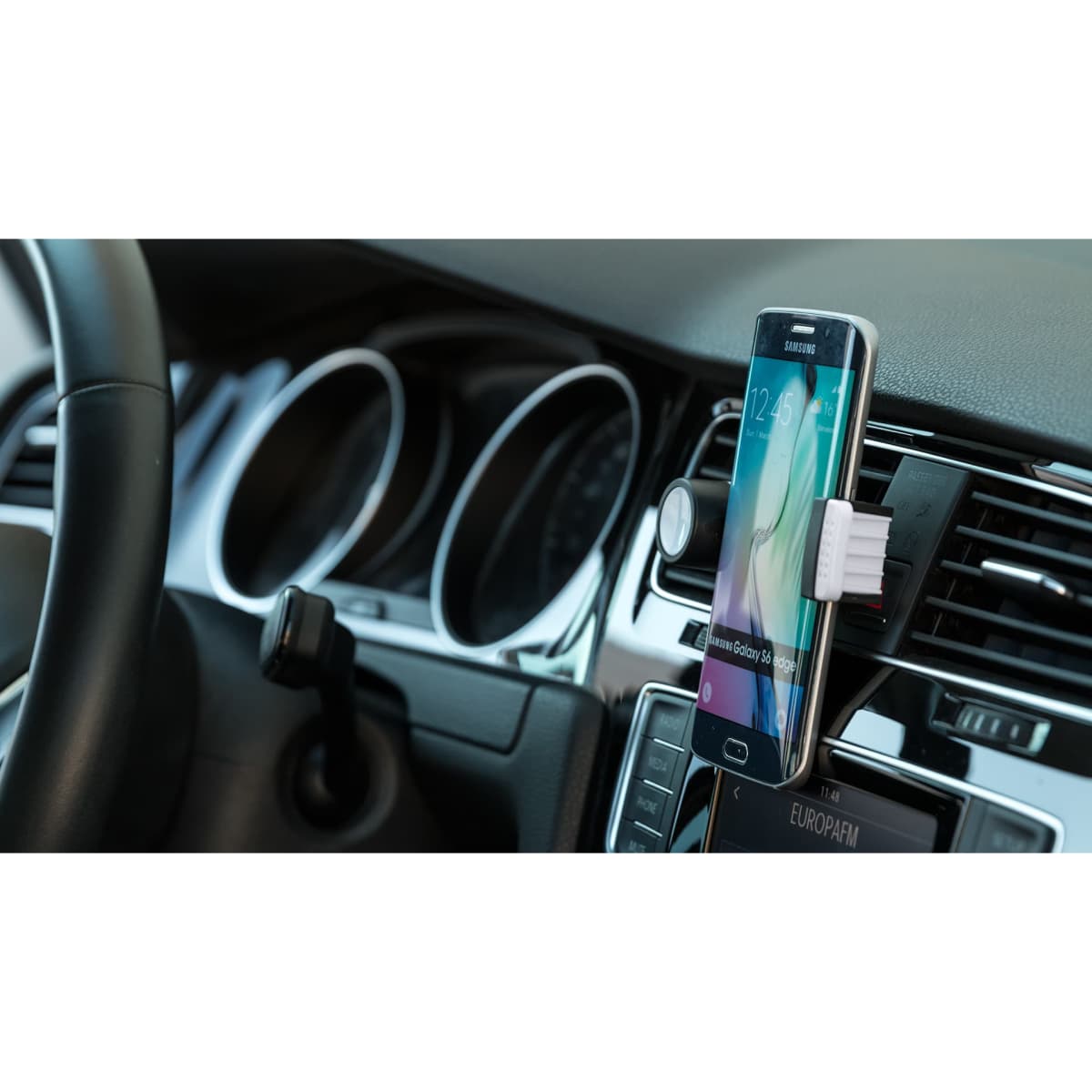 A car dashboard featuring a smartphone in a mount, alongside dashboard controls and dials.