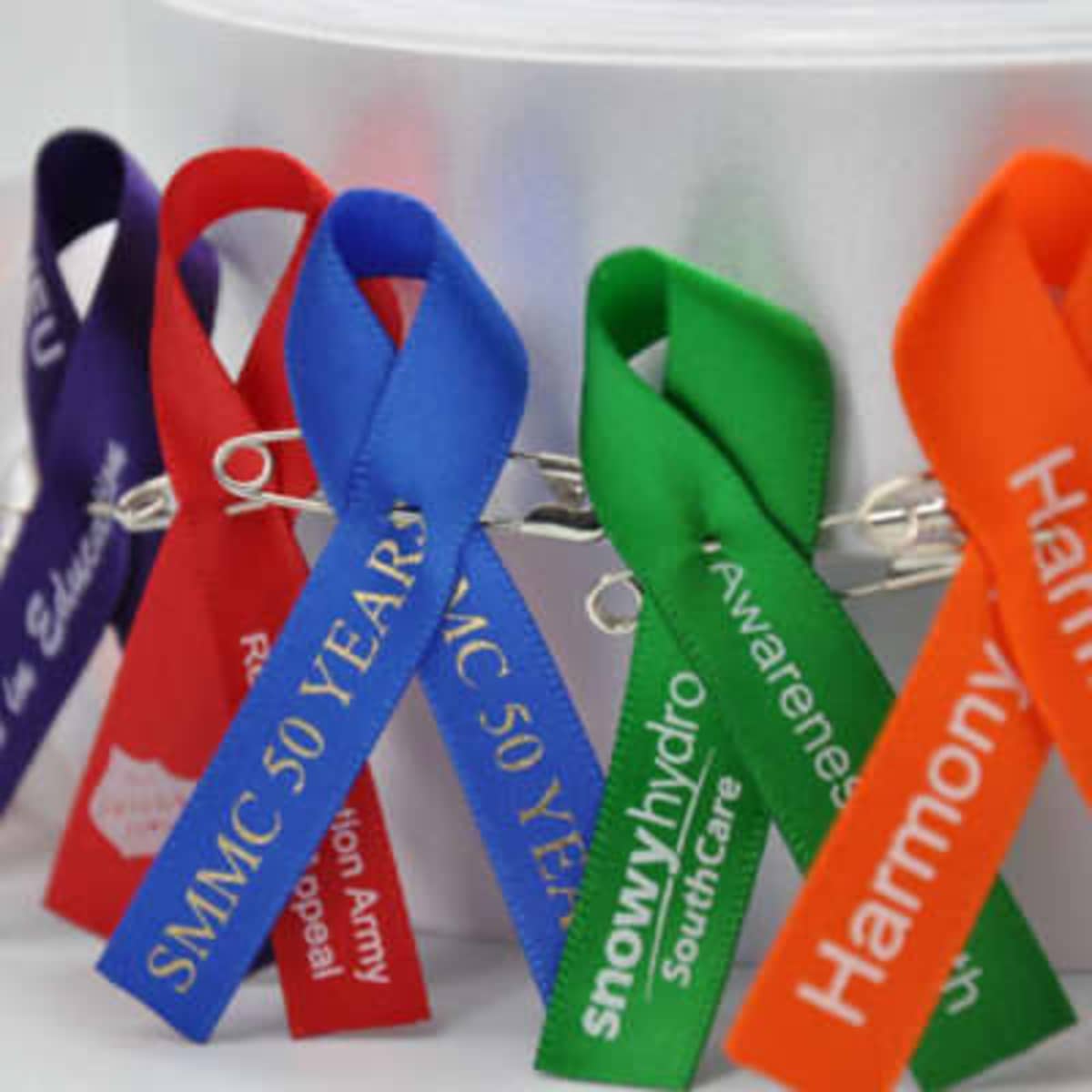 A collection of awareness ribbons in various colours including purple, blue, green, orange, and red, with a silver backing.
