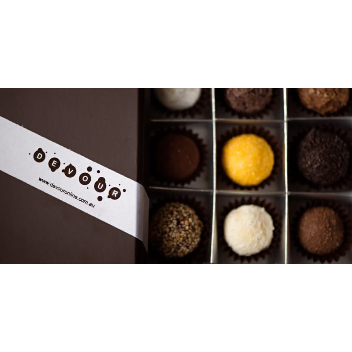 A box of assorted chocolates featuring different colours and textures, with a branded band across the front.