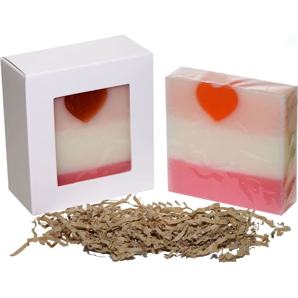 A soap box with a clear window, featuring a layered pink and white soap with a heart shape on top, surrounded by shredded paper.