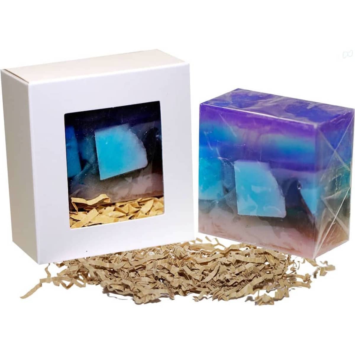 A soap bar in a box featuring blue and purple hues, with shredded paper filling the bottom. The box has a window.