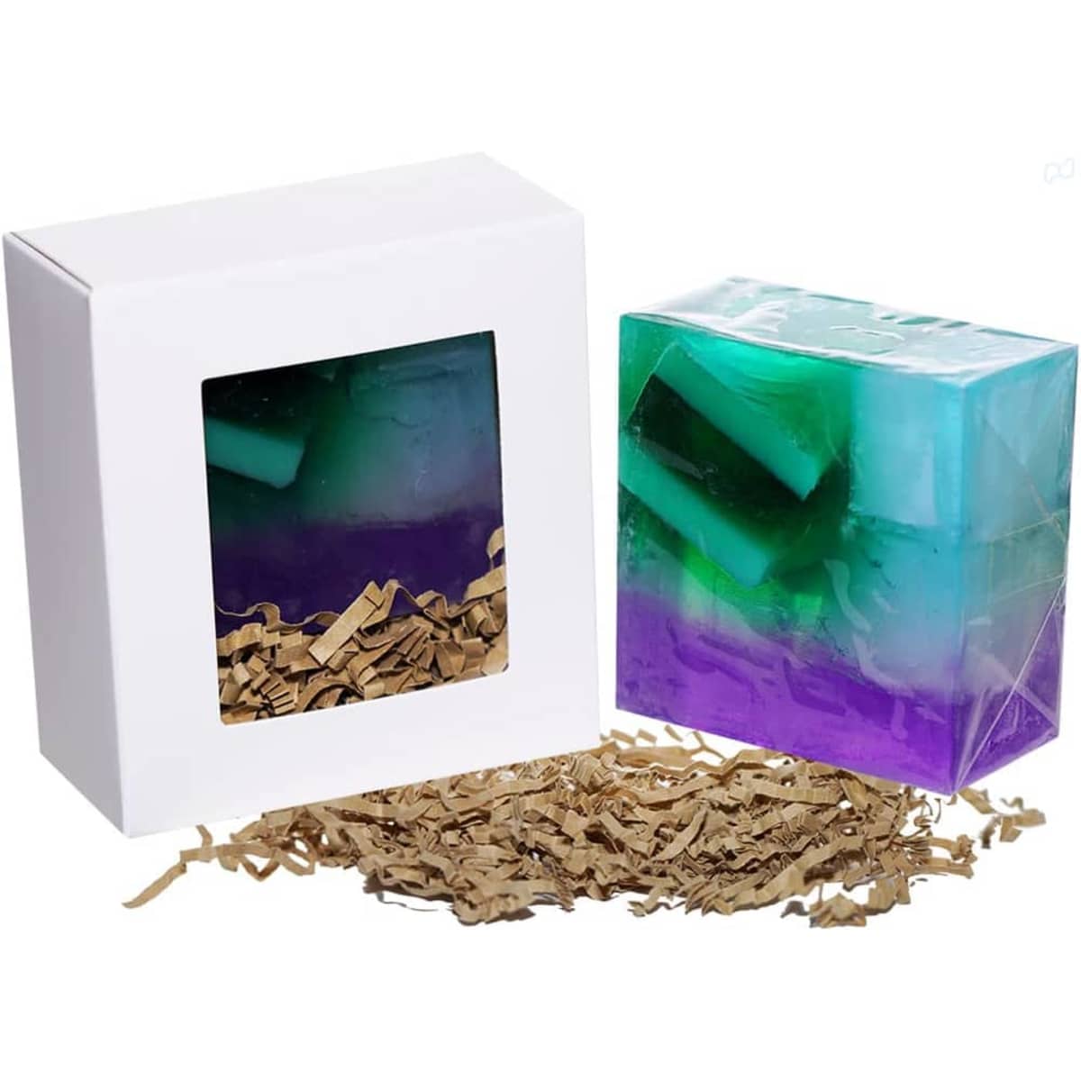 A soap bar with a gradient of blue and purple sits next to its white box, surrounded by shredded paper.