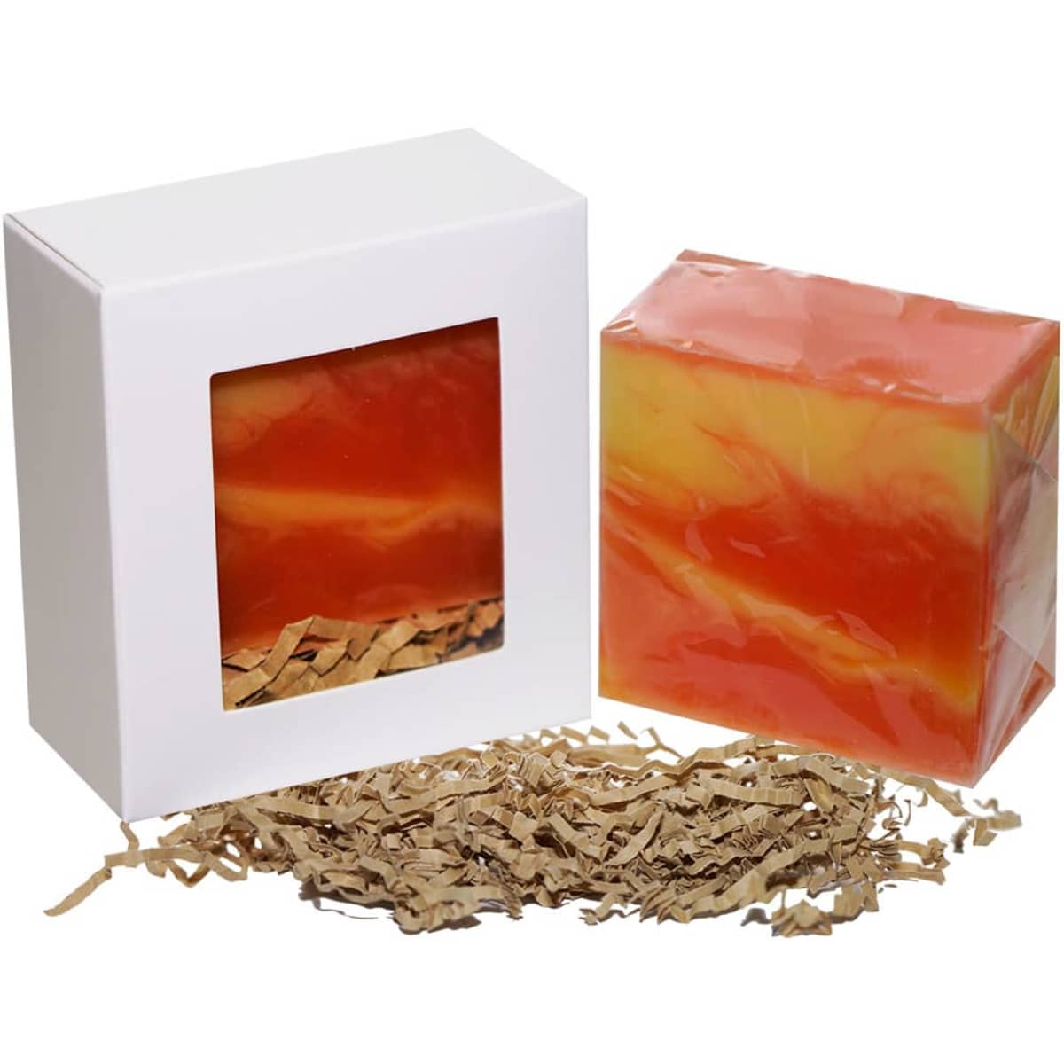 A soap product in an orange and yellow swirl, packaged in a white box with window, alongside brown shredded paper.