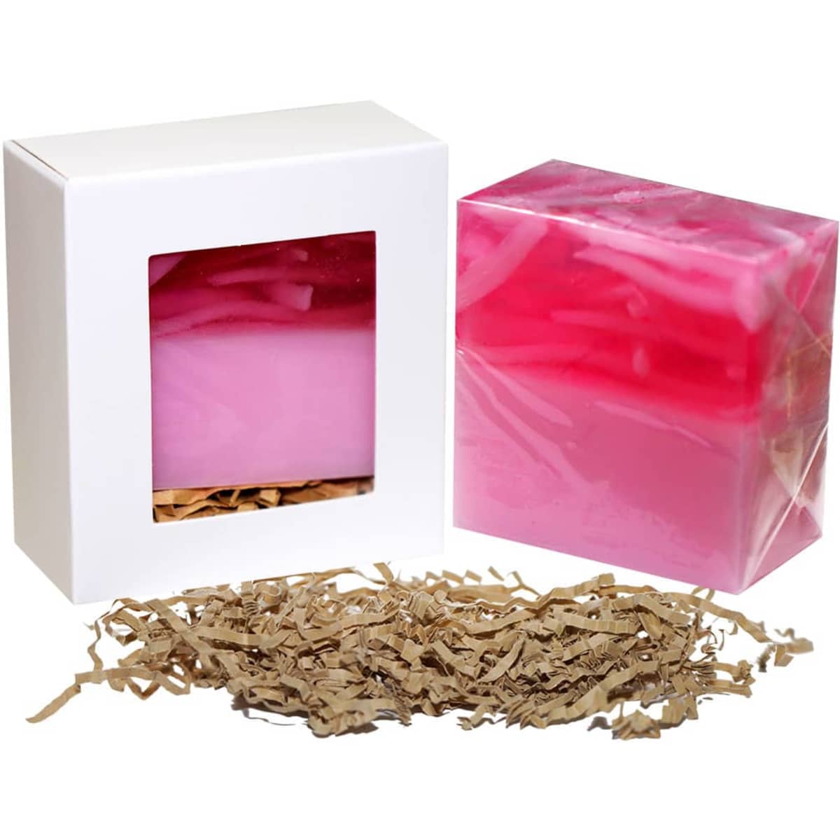 A pink and red soap bar in a clear box, with shredded brown paper underneath for packaging. The box has a logo.