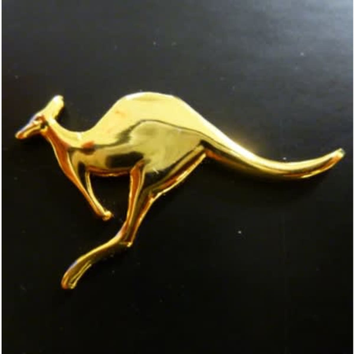 A gold kangaroo figurine with a shiny finish, set against a black background.