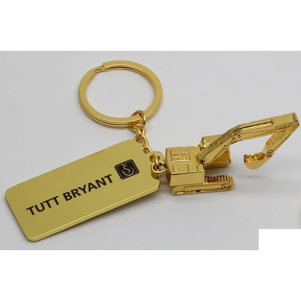 A gold keyring featuring a miniature excavator attached to a rectangular tag with a logo.