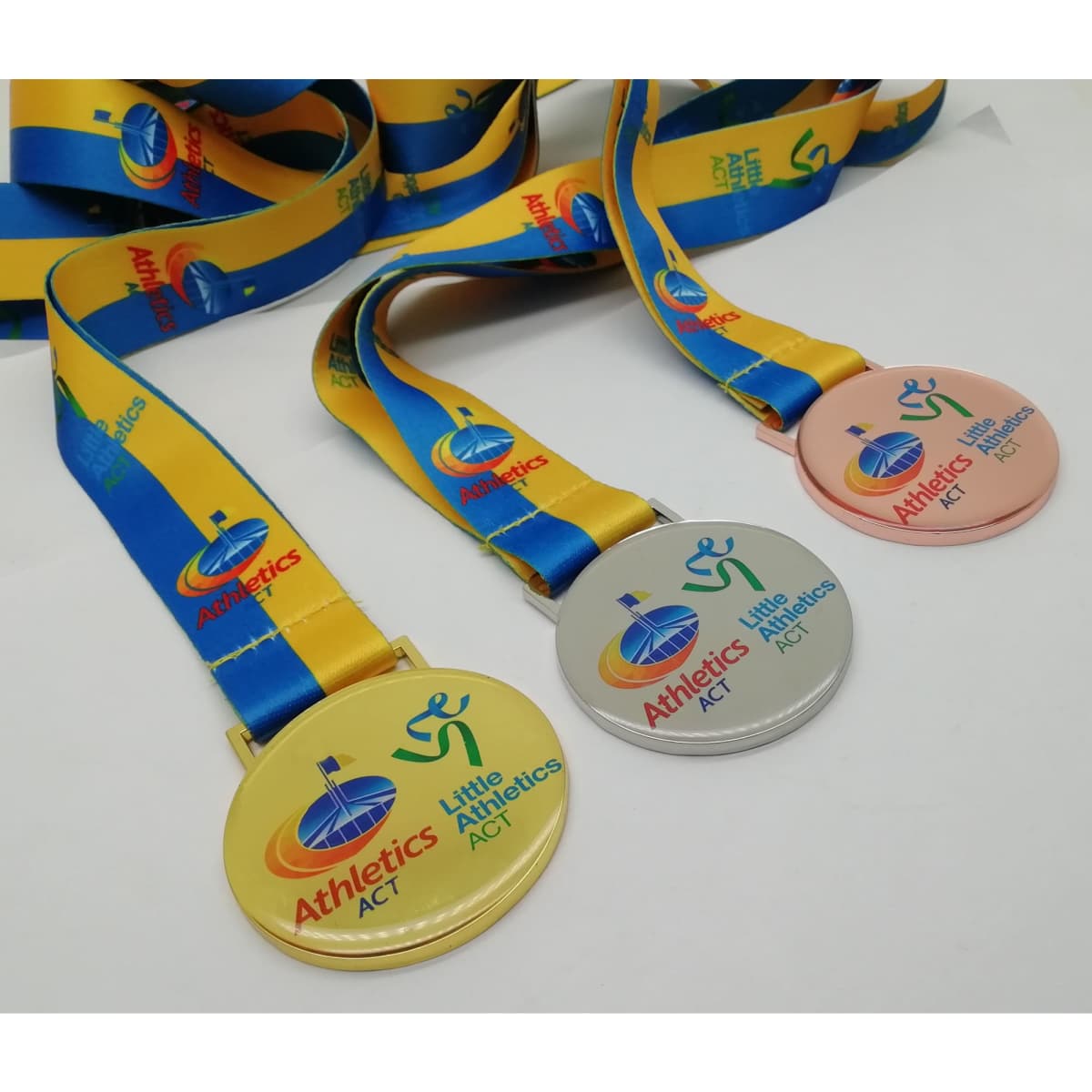 Three printed medals in gold, silver, and bronze with colourful ribbons featuring logos and text.