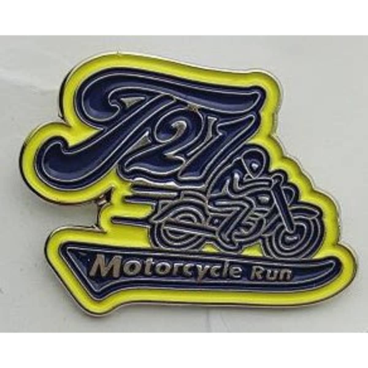 A soft enamel lapel pin featuring a motorcycle design in blue and yellow with a logo. No epoxy finish.