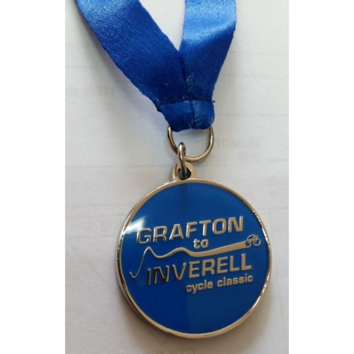 A blue soft enamel medal with an epoxy finish, featuring a silver loop and ribbon. It includes a logo and text.