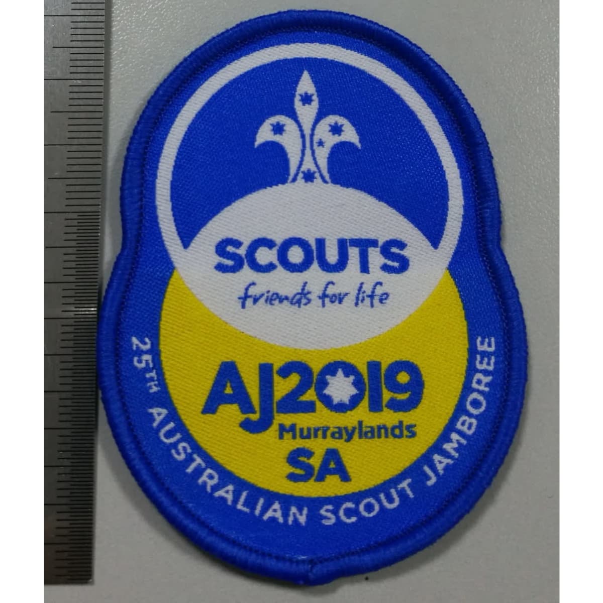 A blue and yellow woven badge featuring a floral design, with a logo and text indicating a scout jamboree event.