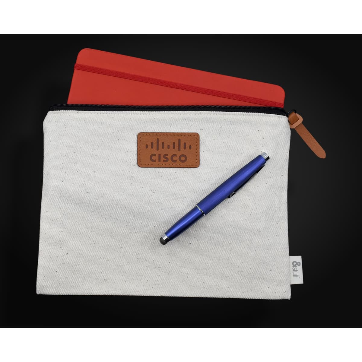 A cream conference bag featuring a brown logo patch, a red tablet cover, and a blue pen.