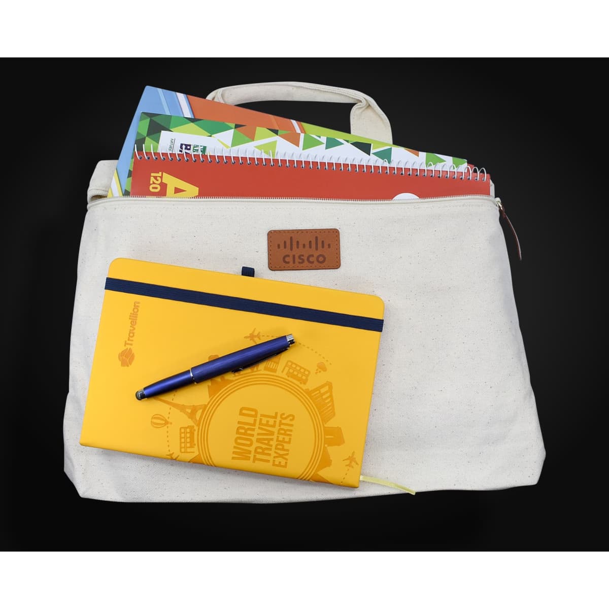 A cream-coloured conference bag with a handle, containing notebooks and a blue pen, featuring a logo.