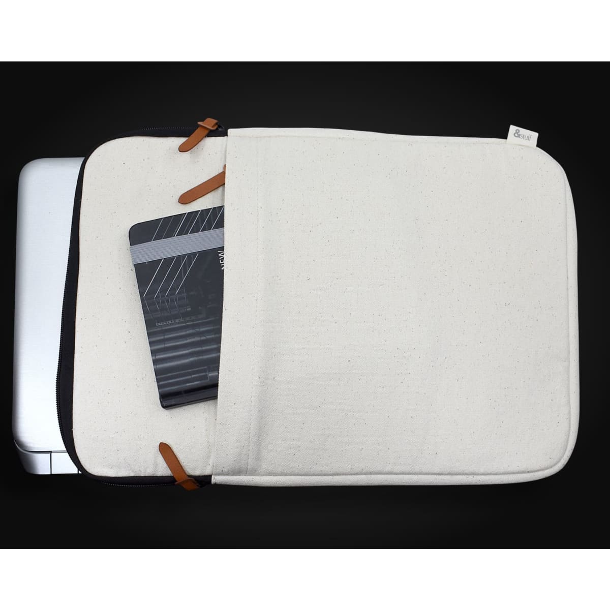 A cream-coloured laptop sleeve with leather accents, showing a partially open compartment and a notebook inside.