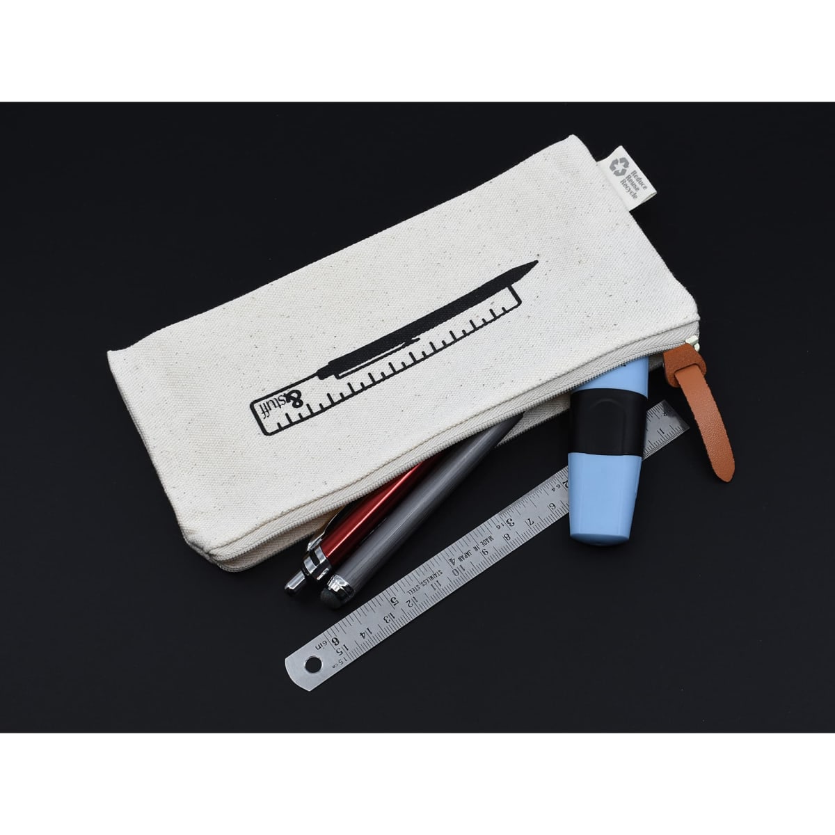 A cream-coloured pencil case with a ruler graphic, containing pens, a highlighter, and a ruler, with a leather zipper pull.