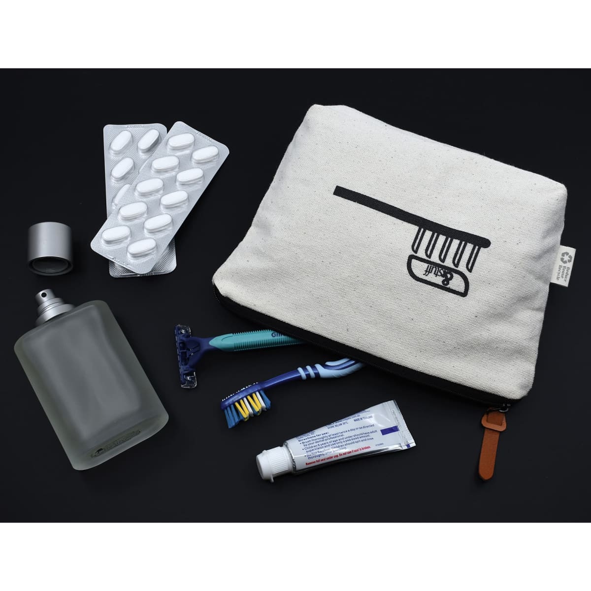 A cream and black toiletry bag with a comb graphic, containing a bottle, razor, toothbrush, and medication strip.