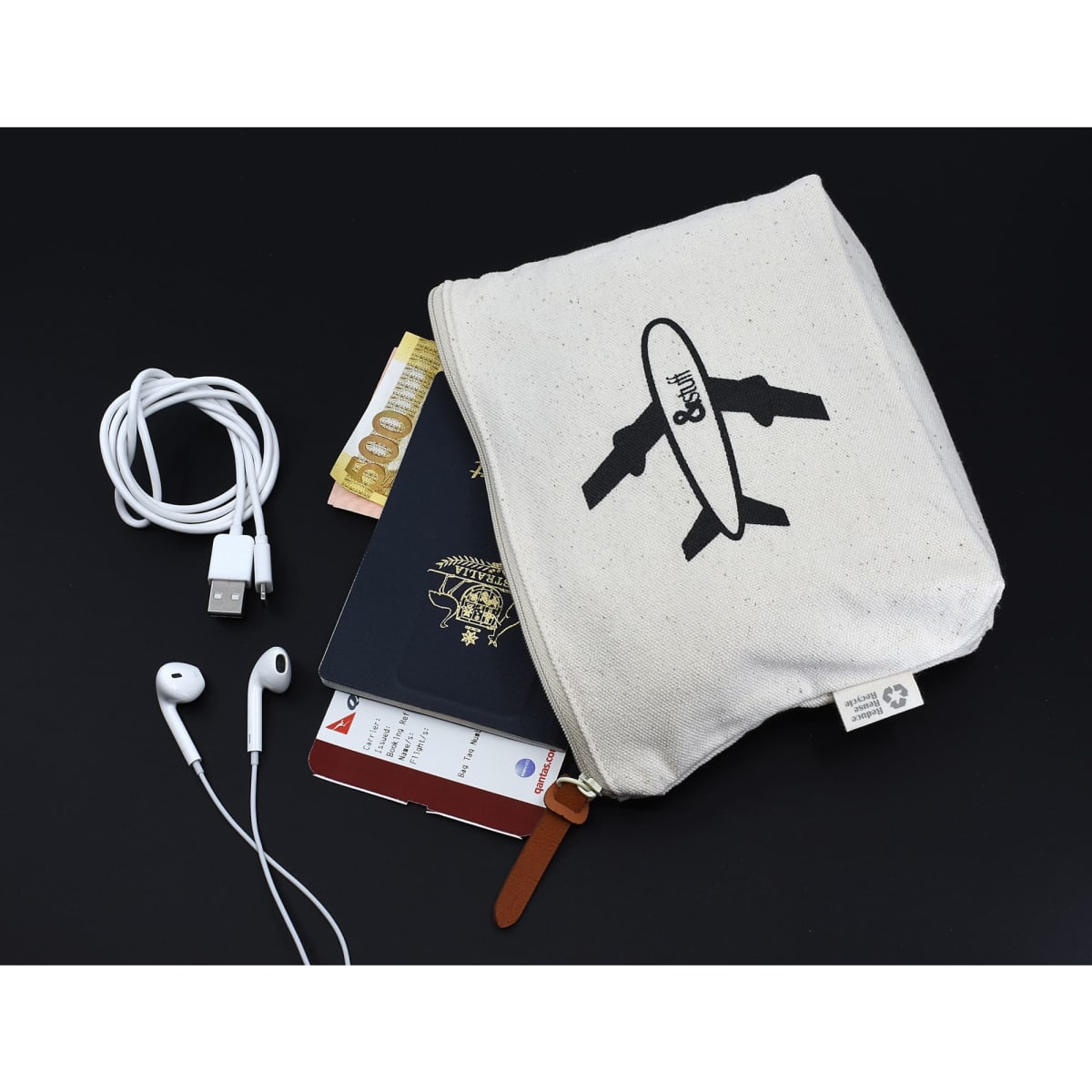 A cream toiletry pouch featuring a logo, containing a passport, currency, earphones, and a charger.