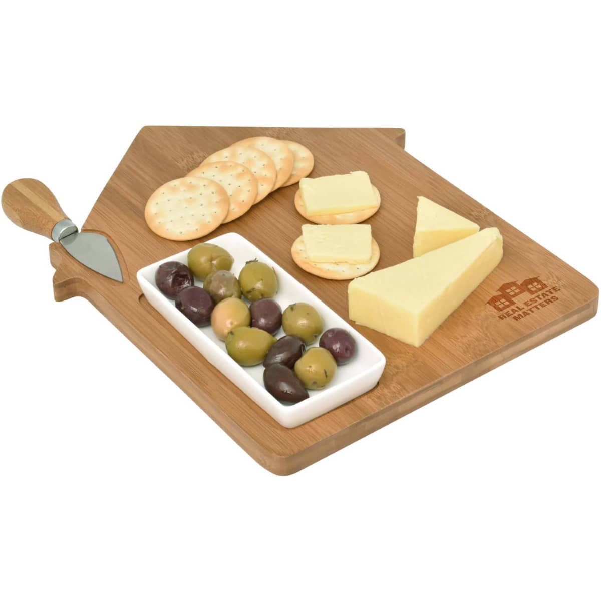 A wooden cheese board shaped like a house, featuring cheese slices, crackers, olives, and a cheese knife.