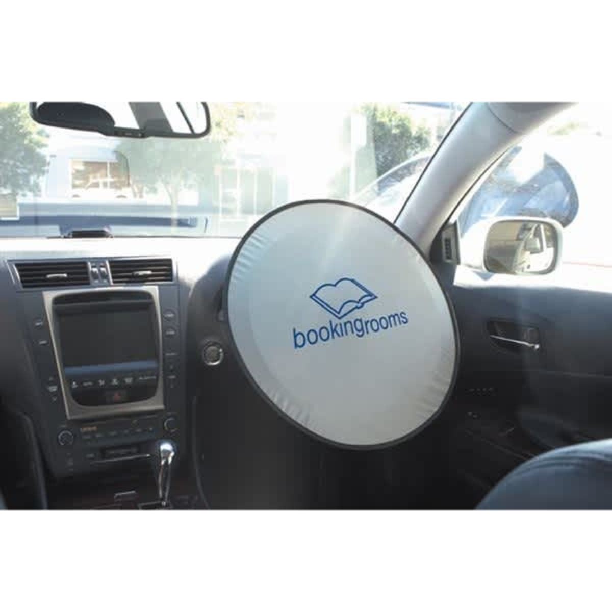 A circular sunshade for a car with a white exterior and a logo, placed on the steering wheel inside a vehicle.