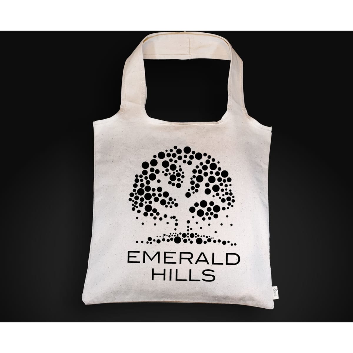 A cream-coloured tote bag featuring a tree design and branding. The bag has shoulder straps and a spacious interior.
