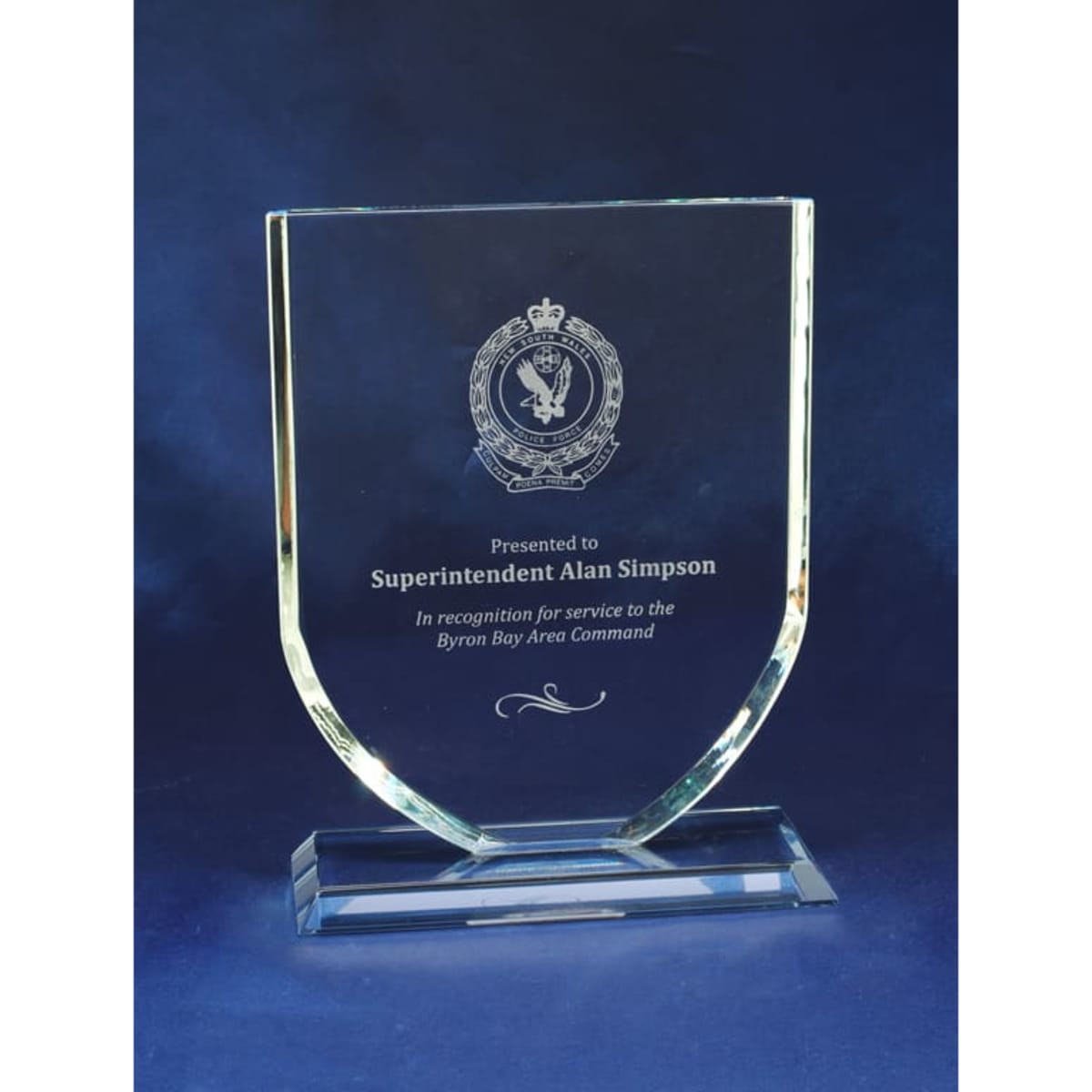 A glass plaque with a clear, angled design, featuring an emblem and engraved text on a blue background.