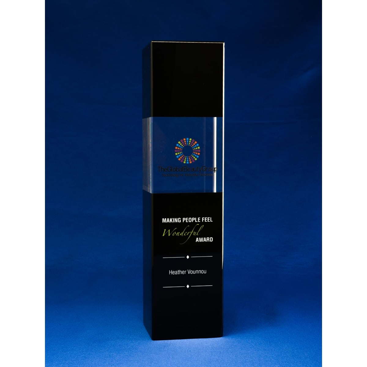 A tall, elegant crystal award featuring a clear top and a black base, with a logo on the front.