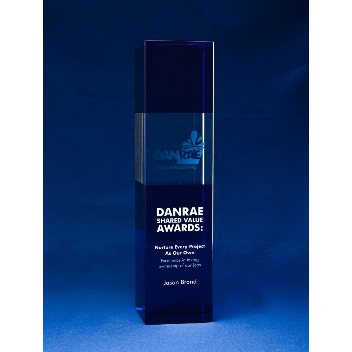 A blue crystal tower award with a sleek design, featuring a logo and engraved text.