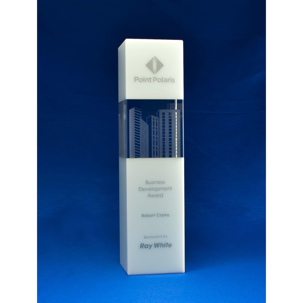 A crystal tower award in clear glass with a city skyline design, against a blue background. It features a logo and text.