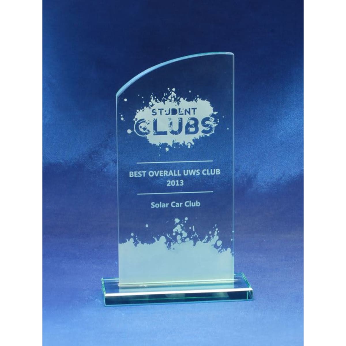 A jade glass trophy with a curved top, featuring a base and an engraved design, against a blue background.
