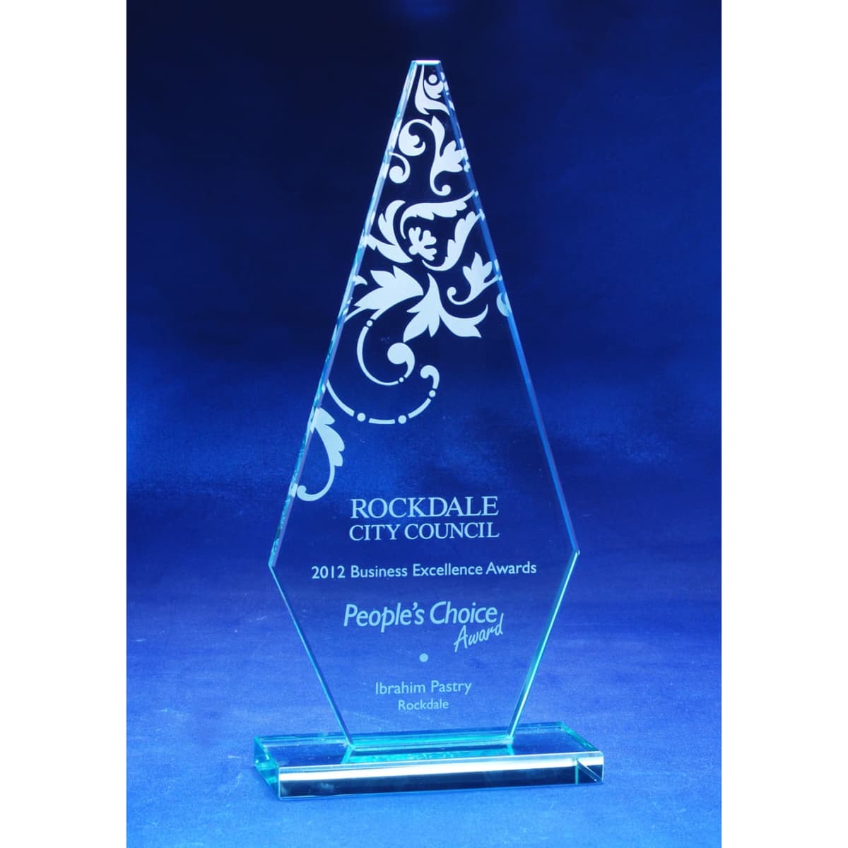 A jade glass trophy with an arrowhead shape, featuring decorative engravings and a base.