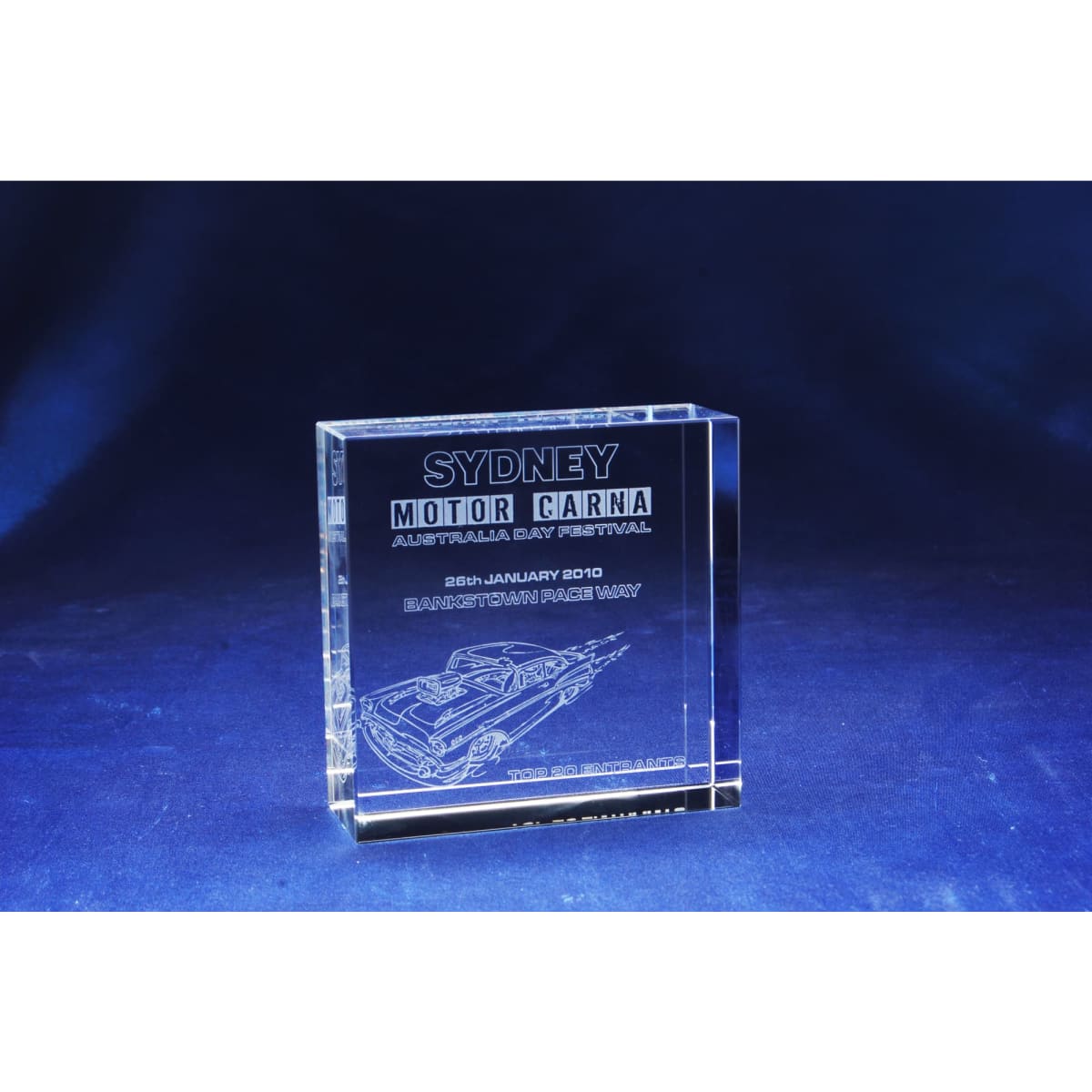 A square optical crystal award featuring etching of a car, with a clear finish set against a deep blue background.