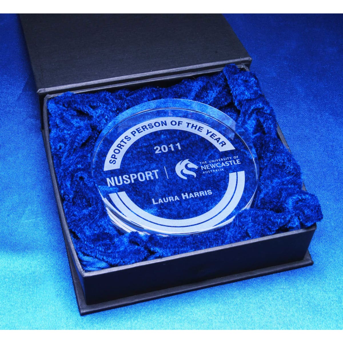 A crystal medallion in a black presentation box, surrounded by blue cushioning material.