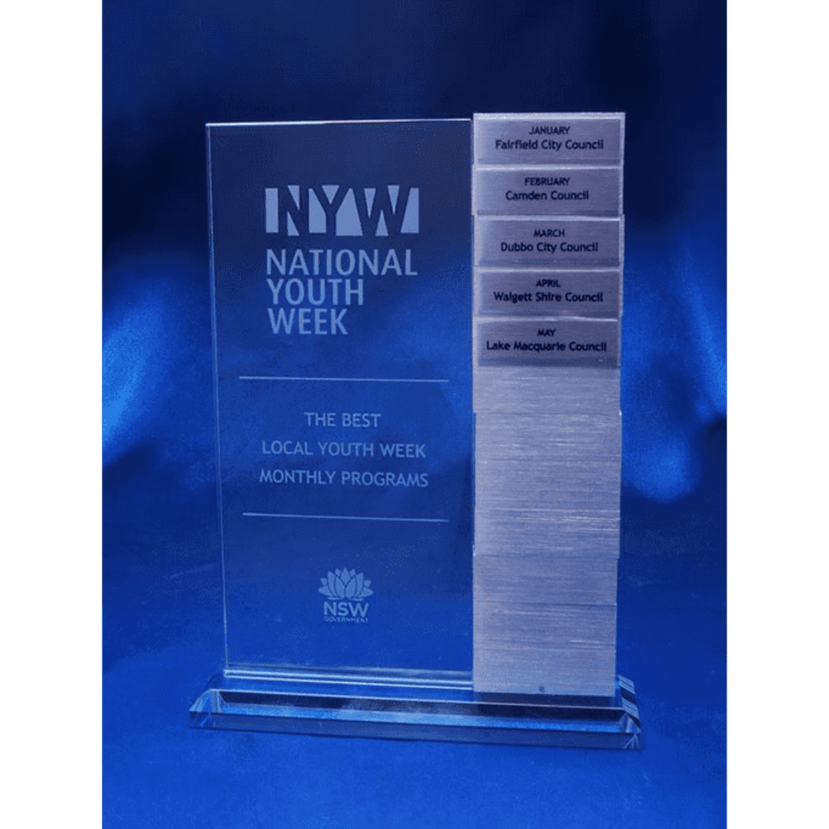 A clear acrylic award with a rectangular base, featuring engraved text and multiple engraved tabs for months and council names.